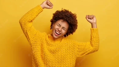 joyful-afro-woman-raises-arms-tilts-head-dressed-casual-knitted-jumper-laughs-from-happiness-celebrates-victory-isolated-yellow_273609-32594